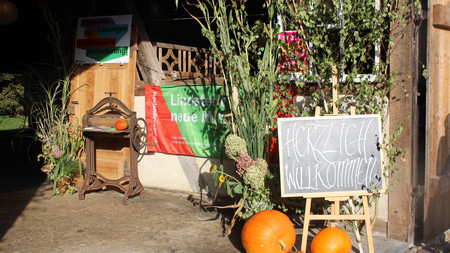 Tafel auf Staffelei mit Schriftzug Herzlich Willkommen vor herbstlicher Dekoration an Eingang einer Scheune