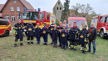 Gruppe der Jugendfeuerwehr in Schutzkleidung steht vor Feuerwehrfahrzeugen und halten T-Shirts