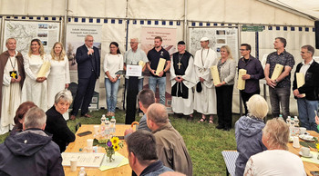 große Gruppe von Personen im Halbkreis vor Publikum stehend, teilweise in mittelalterlichen Kostümen von Geistlichen und Pilgern