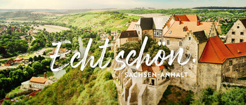 Blick in ein grünes Flusstal mit Burg im Vordergrund und Schriftzug „Echt schön. Sachsen-Anhalt“