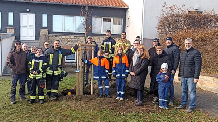 Gruppe von Personen vor einem Gebäude mit einem frisch gepflanzten Baum