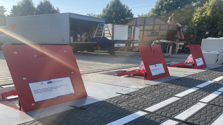 Drei aufgestellte mobile Straßensperren in rot mit Schild zum Hinweis auf EU-Förderung