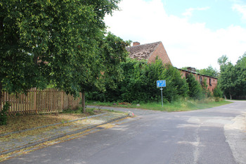 Straße mit grün bewachsenem Gebäude auf der linken Seite und schmaler gepflasterter Zufahrt