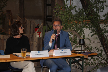 Eine Frau und ein Mann mit Mikrofon an Podiumstisch mit Namensschildern