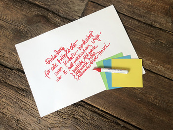 Weißes Blatt mit handschriftlicher Einladung zu Workshop mit drei bunten Klebezetteln und Stift