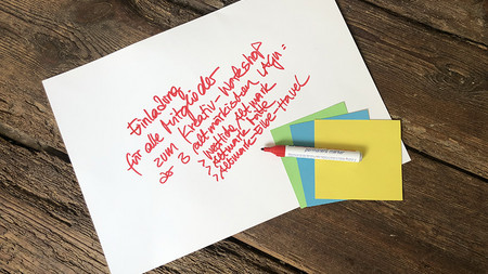 Weißes Blatt mit handschriftlicher Einladung zu Workshop mit drei bunten Klebezetteln und Stift