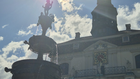 Springbrunnen mit Lüneburger Rathaus und Sonne im Hintergrund 