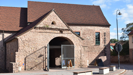 Außenansicht eines aus unterschiedlichen Steinen gemauerten Gebäudes mit großen Torbogen und Schriftzug Stadthalle an der Seite