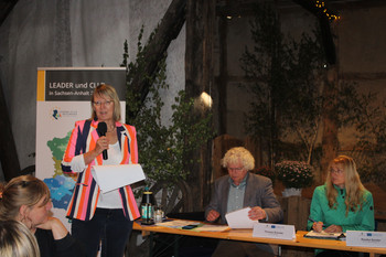 Eine Frau mit Mikrofon vor Publikum redend