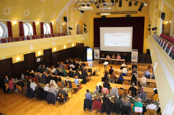 Blick von oben in einen großen Saal mit Konferenzsituation