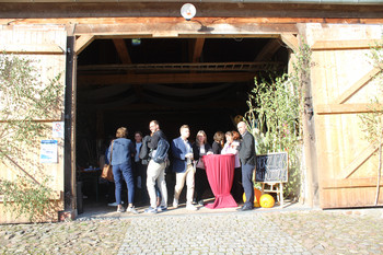 Personengruppen an Stehtisch im Eingangsbereich einer Fachwerkscheune mit geöffnetem Scheunentor