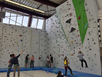 Kletterwand mit verschiedenen bunten Griffen mit kletternden und stehenden Personen