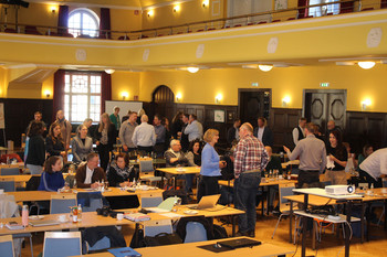 Blick in einen Saal mit mehreren Personengruppen im Gespräch